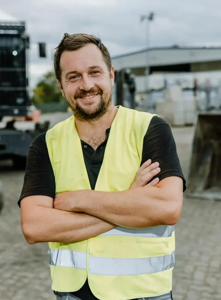 Aufnahme von einem lächelndem Mitarbeiter in Warnweste auf einem Entsorgungsgelände